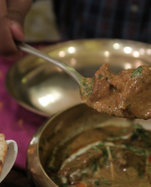 印度餐厅的菜肴，murgh methi masala chicken tikka咖喱食谱(香料香料的masala chicken with葫芦巴和奶油)，男子为自己服务，并把自制的烤鸡与勺子照片，大蒜馕饼，金属塔利菜和盘子图片下载