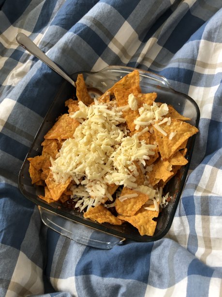 不健康的零食/垃圾食品在床上吃，在被子下看电视，芝士玉米片薯片/橙子玉米片与番茄莎莎和磨碎的马苏瑞拉奶酪融化的照片图片下载