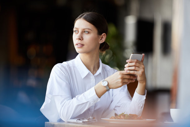 沉思、目标坚定的年轻女商人，戴着手表坐在桌边，在餐厅等同事时发短信图片下载
