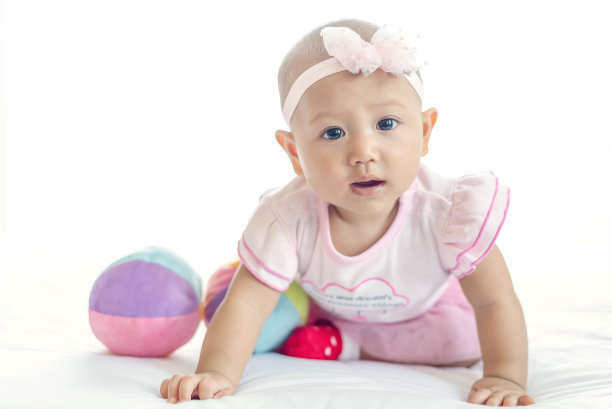 7个月大的亚洲小女孩，穿着粉红色的衣服，躺在白色的床上看着照相机。图片下载