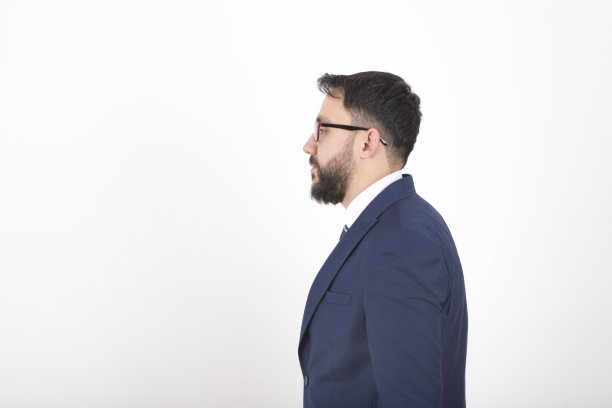 侧面视图的年轻商人在深蓝色西装看着远离白色的背景图片下载