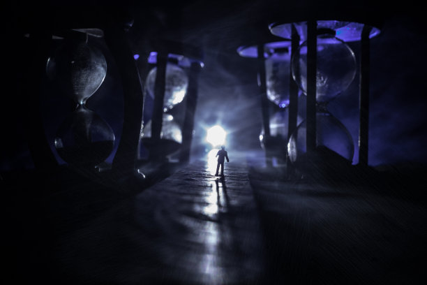 时间的概念。一个男人的剪影站在沙漏中间，在黑暗的背景上有烟雾和灯光。超现实主义的装修图片图片下载