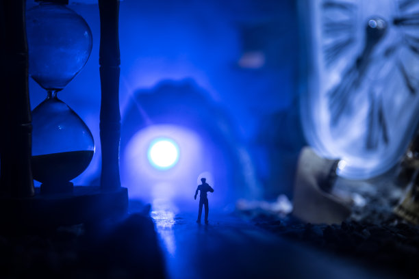 时间的概念。一个男人的剪影站在沙漏中间，在黑暗的背景上有烟雾和灯光。超现实主义的装修图片图片下载