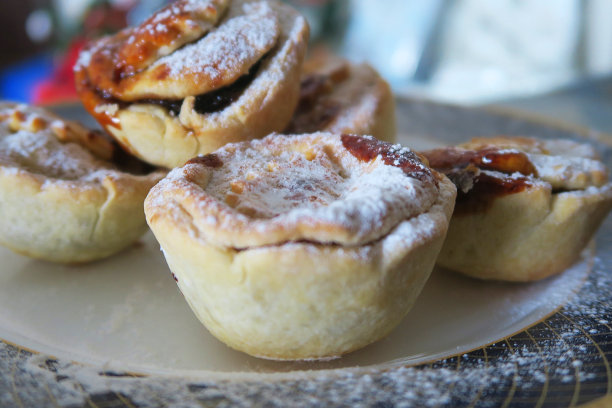 背景是圣诞树的自制肉馅饼，模糊的仙女灯，酥皮上撒着糖霜，用肉馅饼和酥皮混合物烘焙的肉馅饼食谱，盘子上的照片显示肉馅饼馅料和可食用的酥皮图片下载