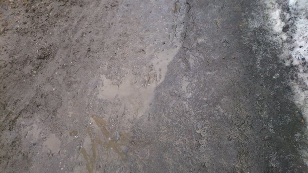 在深冬，路边的积雪正在融化，泥土覆盖着积雪，形成水坑图片下载