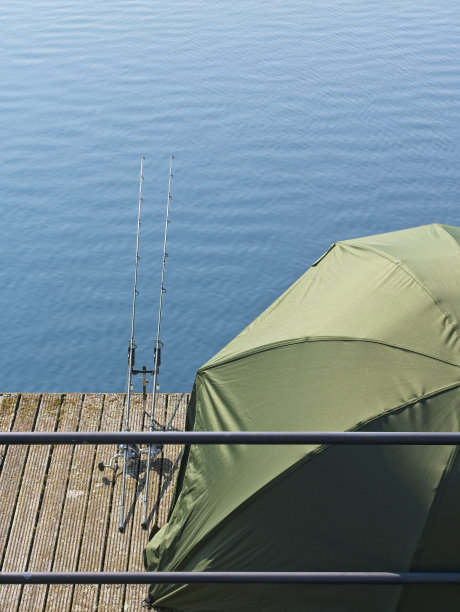湖边的绿色帐篷旁有两根钓鱼竿。放松的假期的形象。图片下载