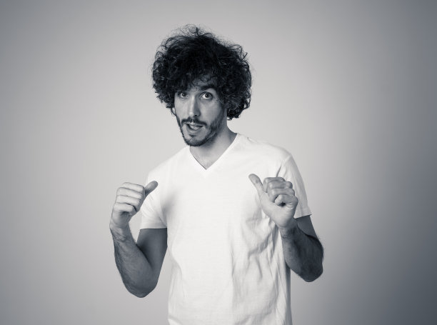 照片中，年轻的千禧一代男性带着一头熊，头发浓密，面带微笑，做着有趣而友好的手势。在中性背景下隔离。人的表情和广告的概念。图片下载