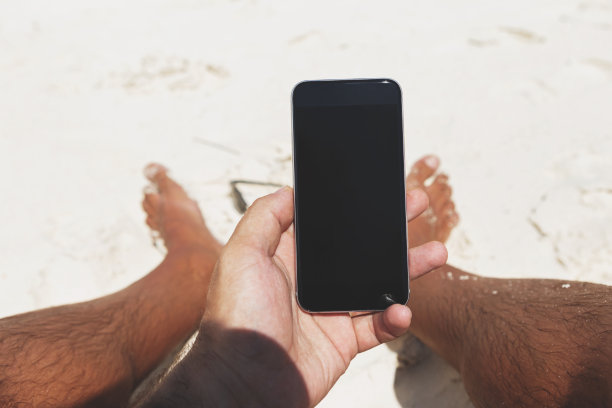 夏天的海滩上，男性手握手机黑屏图片下载