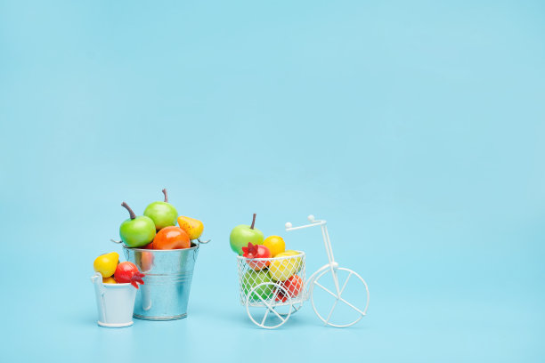 白色钢丝自行车和一个装满迷你水果的篮子。靠近装着蔬菜和水果的桶。蓝色背景。收获和运送果蔬的理念。图片下载