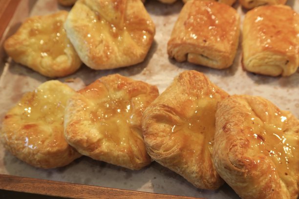 在酒店餐厅自助面包房自制新鲜烘焙的法式早餐馅饼，巧克力巧克力牛角面包照片，涂满果酱的杏子和苹果糕点，放在木托盘上的金黄色酥皮糕点，烤羊皮纸防油纸图片下载