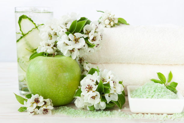 盛开的苹果树花、冷饮、青苹果、香海盐、毛巾。水疗、美容、健康沙龙的概念。特写照片上的白色木制背景，选择性聚焦图片下载