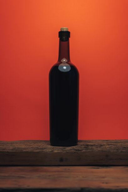 旧橡木木桌上放一瓶红酒，背景是珊瑚色。图片下载