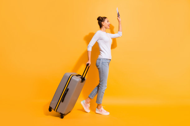 侧面的全身尺寸的照片，女士等待飞机出租车酒店在机场拿着文件，在手里的行李手提箱在浅套头衫蓝色牛仔裤孤立在充满活力的背景图片下载