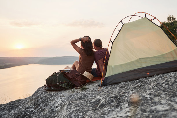 这是一对快乐的夫妇在徒步旅行时坐在帐篷里看湖的照片。旅行生活冒险度假概念图片下载