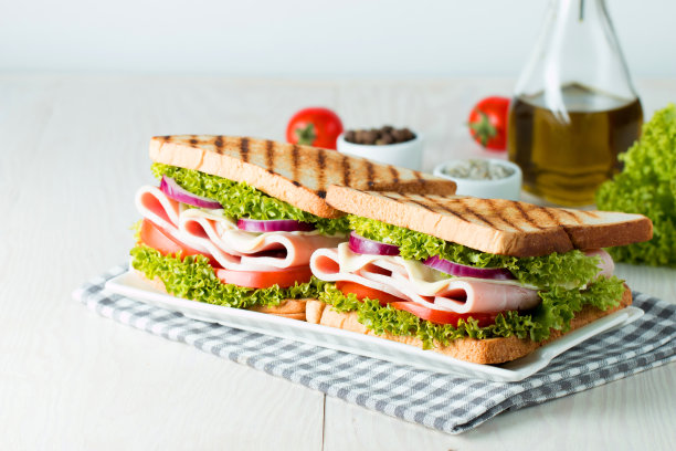 俱乐部三明治的特写照片。三明治与肉，火腿，意大利腊肠，沙拉，蔬菜，生菜，番茄，洋葱和芥末在新鲜的黑麦面包切片在木制背景。橄榄背景。图片下载