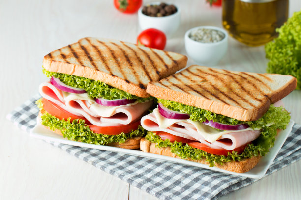 俱乐部三明治的特写照片。三明治与肉，火腿，意大利腊肠，沙拉，蔬菜，生菜，番茄，洋葱和芥末在新鲜的黑麦面包切片在木制背景。橄榄背景。图片下载