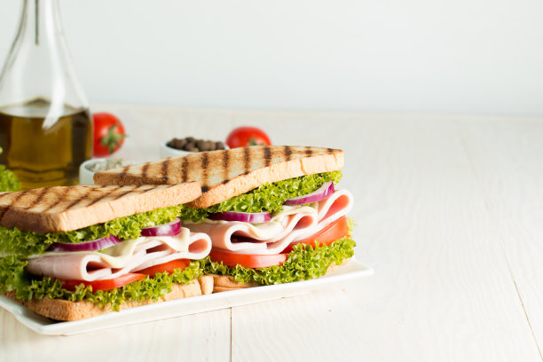 俱乐部三明治的特写照片。三明治与肉，火腿，意大利腊肠，沙拉，蔬菜，生菜，番茄，洋葱和芥末在新鲜的黑麦面包切片在木制背景。橄榄背景。图片下载
