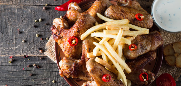烧烤鸡翅与薯条和啤酒的特写照片。烤肉配酱汁，番茄酱，蛋黄酱。快餐和垃圾食品的概念。图片下载
