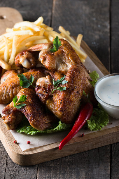 烧烤鸡翅与薯条和啤酒的特写照片。烤肉配酱汁，番茄酱，蛋黄酱。快餐和垃圾食品的概念。图片下载
