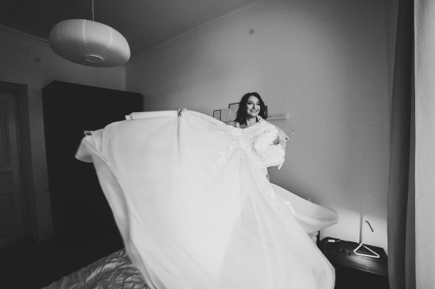 新娘手里拿着婚纱，在床上旋转，和她一起旋转。风格复古优雅的连衣裙与蕾丝。早上的婚礼准备工作。黑白照片。图片下载
