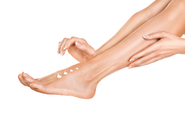 迷人的女人在白色的背景上把奶油涂在她的腿上。图片下载