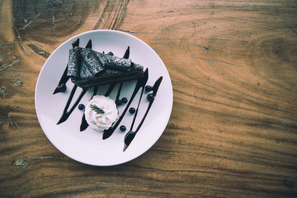 美味的黑巧克力奶油蛋糕，白色的圆盘放在木桌上;俯视图照片图片下载
