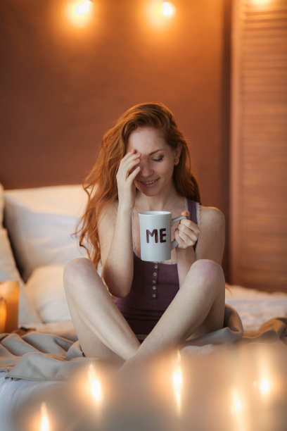 年轻美丽的女人的肖像，她的手捧着咖啡早上寒冷的冬天时间在她的白色卧室。快乐愉悦放松在寒冷的冬天化妆生活理念。图片下载