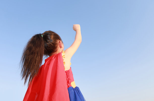 超级英雄小女孩站在日落的天空背景上飞行。小孩超级英雄概念。后面的观点。图片下载