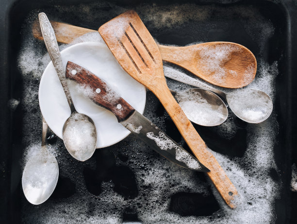 汤sud洗涤。一个盘子，一把刀，木制的厨房抹刀和勺子，放在一个黑色的烤箱托盘上，放入洗涤剂泡沫。洗碗的概念。前视图。图片下载