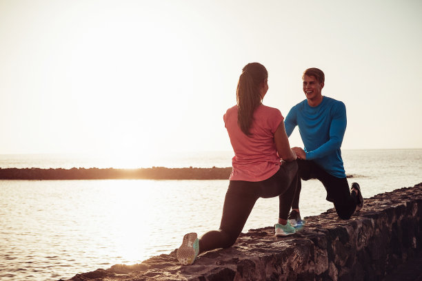 适合夫妇户外伸展和训练腿-运动的年轻人在海滩下做运动-运动，健身和健康的生活方式的概念图片下载