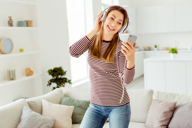 近距离的照片美丽的她她的女士手臂手拿电话读单词歌曲耳罩耳朵非常高兴时髦的穿着牛仔裤牛仔条纹套头衫衣服明亮舒适的公寓房子客厅在室内图片下载