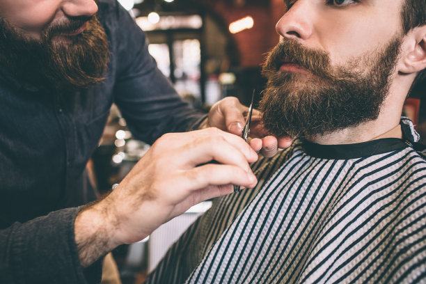 大胡子男人的特写。理发师正在给他剪胡子。这个过程虽然缓慢，但充满信心，值得一试。减少视图。图片下载