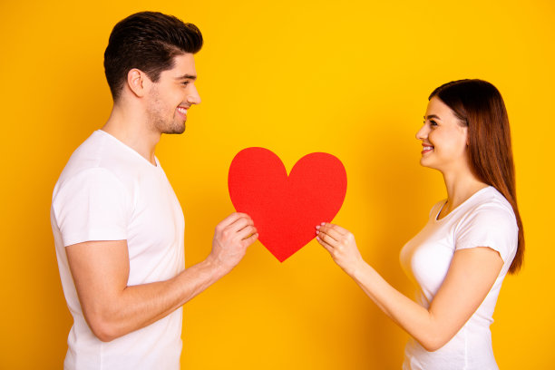 近距离的侧面资料照片惊人的美丽，她，她，他，他，他的男人，女士，看眼睛可爱的手，手臂，大的纸，心的人物，明信片，穿休闲的白色t恤孤立的黄色背景图片下载