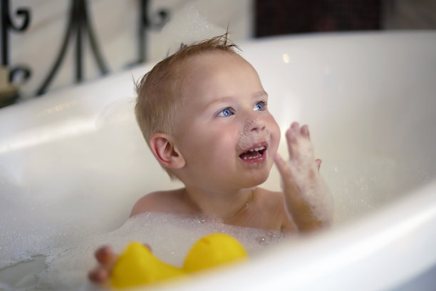 可爱的白种蓝眼睛男婴在浴缸里哭，因为他的脸上和头上有泡沫;手里拿着黄色的玩具鸭子。图片下载