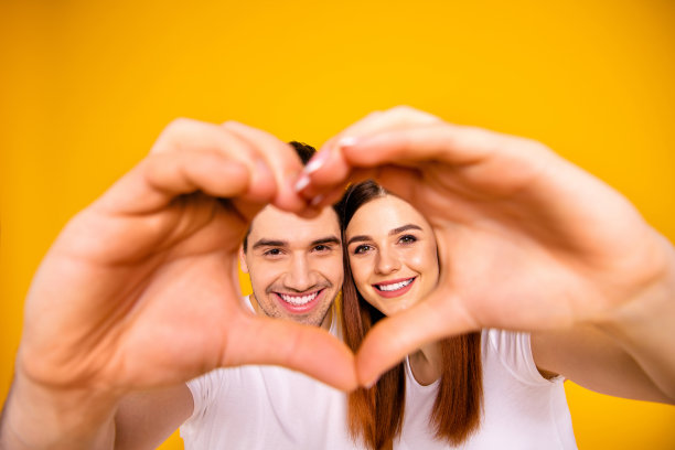 近距离的照片惊人的漂亮，她，她，他，他，他的男人，女士，双手，手臂，手指，使心形的人物，脸，里面的形式，刚刚结婚，浪漫的心情，穿着休闲的白色t恤，套装孤立的黄色背景图片下载