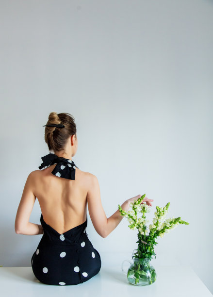 穿着黑色圆点连衣裙的年轻女子坐在马提奥拉鲜花旁边的一张桌子上图片下载