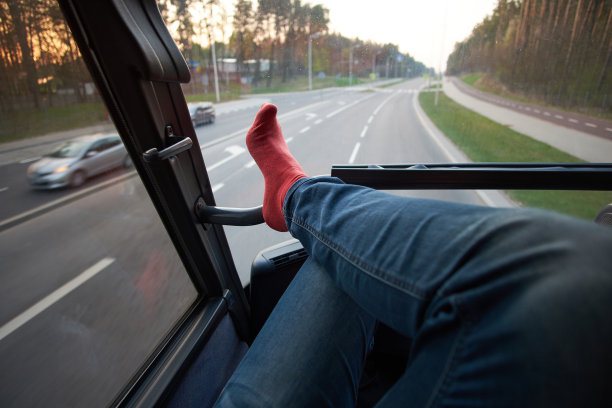 在公共汽车旅行中，放松的游客在车窗上的脚图片下载