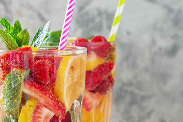 特写两杯加吸管的柠檬水。新鲜健康的饮料，柠檬，草莓和覆盆子。照片与文本空间，复制空间。图片下载