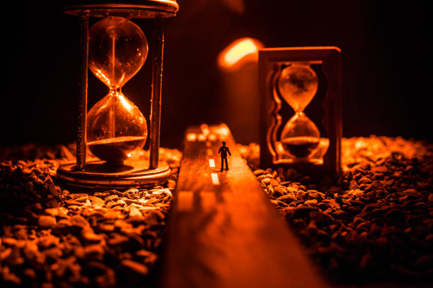 时间的概念。一个男人的剪影站在沙漏中间，在黑暗的背景上有烟雾和灯光。超现实主义的装修图片图片下载