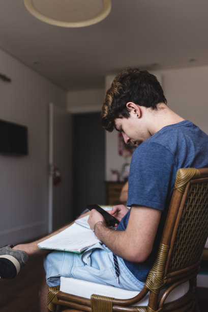 一个十几岁的男孩在做作业的时候用手机图片下载