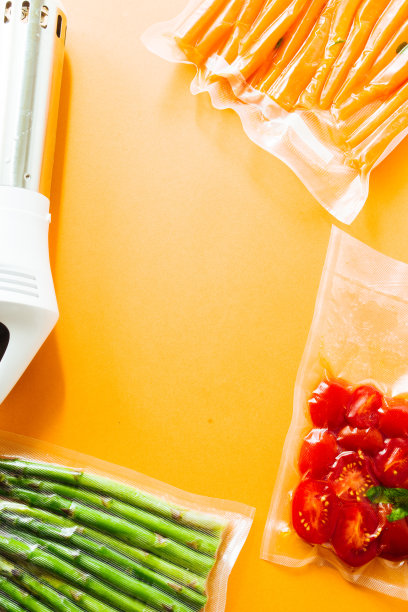 真空密封的蔬菜，胡萝卜，芦笋，西红柿，在一个橙色的背景俯视图，准备与真空蒸煮机，一个自动真空封口机和一个rooner图片下载