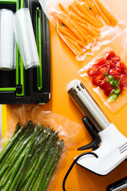 真空密封的蔬菜，胡萝卜，芦笋，西红柿，在一个橙色的背景俯视图，准备与真空蒸煮机，一个自动真空封口机和一个rooner图片下载