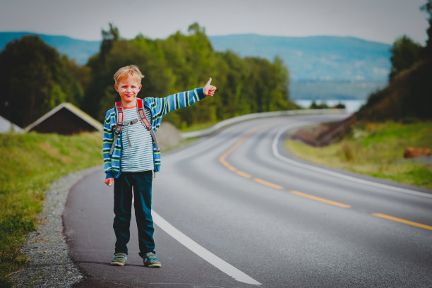 可爱的小男孩背着双肩包在路上旅行，展示着等待车的标志图片下载