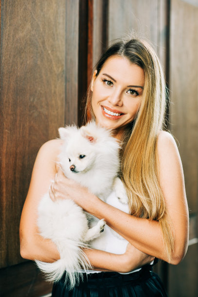 户外肖像快乐的年轻女子抱着白色博美犬狗图片下载