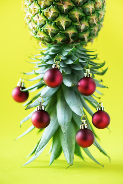 用菠萝和红色的小装饰品做成的创意圣诞树，在黄色的背景上，复制空间。贺卡，装饰新年晚会。节日的概念。图片下载