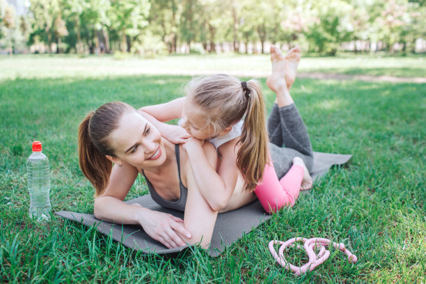 一张女孩们一起玩乐和放松的照片。小女孩正躺在她妈妈的背上。她正看着她。女人很高兴地看着她的孩子。瑜伽和普拉提概念。图片下载