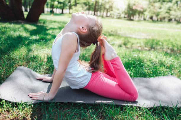 一个柔韧的女孩用她的腿的末端到达她的头的图片。她正在外面的公园里做运动。瑜伽和普拉提概念。图片下载