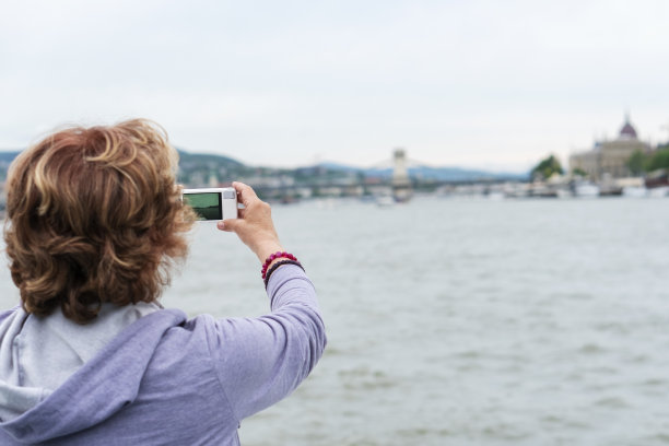 一位年长的妇女在一艘游轮的甲板上拍摄一座城市图片下载