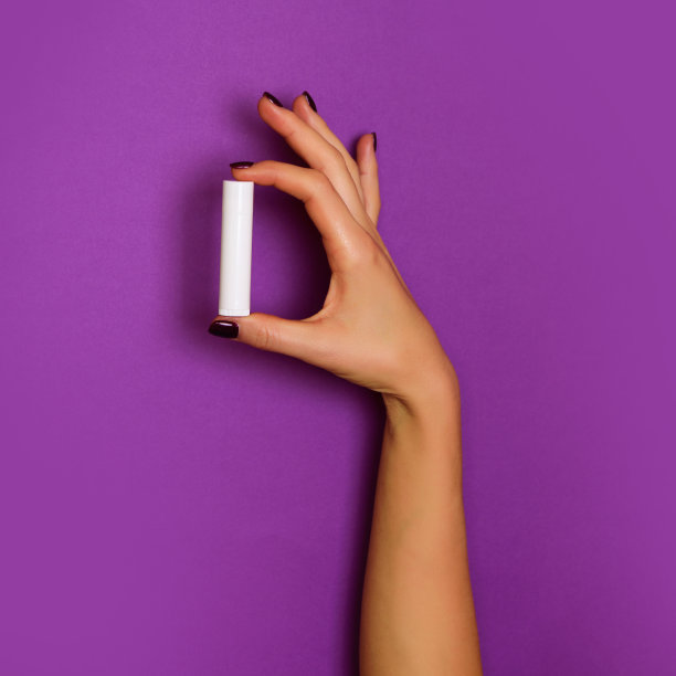 女人的手拿着白色的化妆品瓶在紫罗兰的背景。横幅。护肤，纯美，身体护理理念。广场的作物图片下载