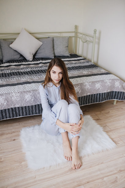 女孩醒了，穿着睡衣坐在她房间的床上。时尚的灰白色内部。图片下载